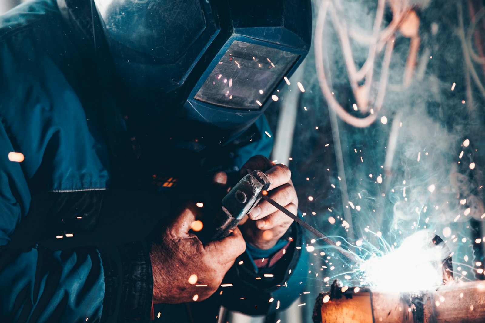 A welder joining steel pipe, with sparks around the arc
